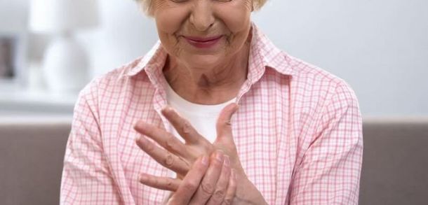 An elderly woman is sitting on a couch holding her hands together.