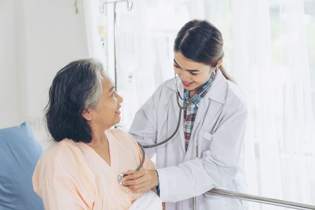 a doctor is listening to an elderly woman 's heart with a stethoscope .