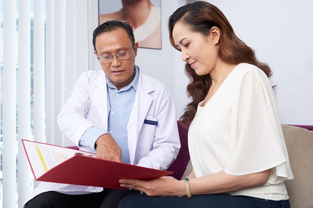 a doctor and a woman are sitting on a couch looking at a clipboard .