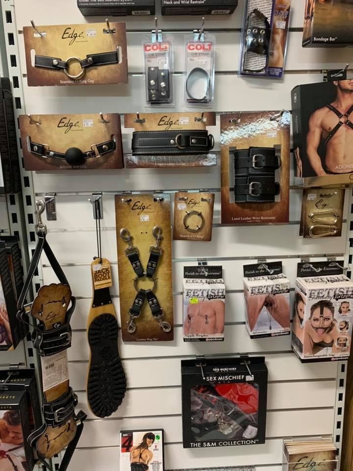 Retail wall display featuring various black leather adult toys, restraints, masks, and sensory accessories for sale — A Bit Cheeky The Adult Store In Lismore, NSW