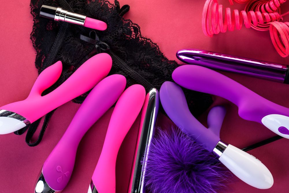 A collection of vibrators in shades of pink and purple, with black lace and accessories, arranged on a bright red background — A Bit Cheeky The Adult Store In Lismore, NSW