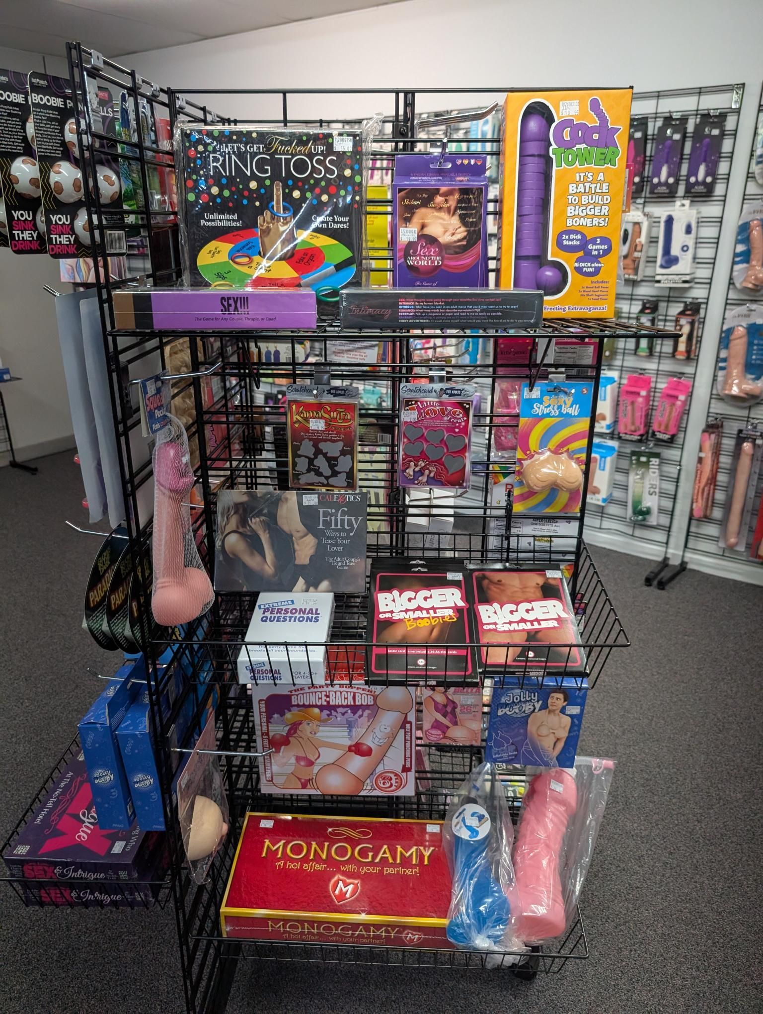 A wire rack display in a retail store showcasing various adult novelty items, games, and accessories — A Bit Cheeky The Adult Store In Lismore, NSW