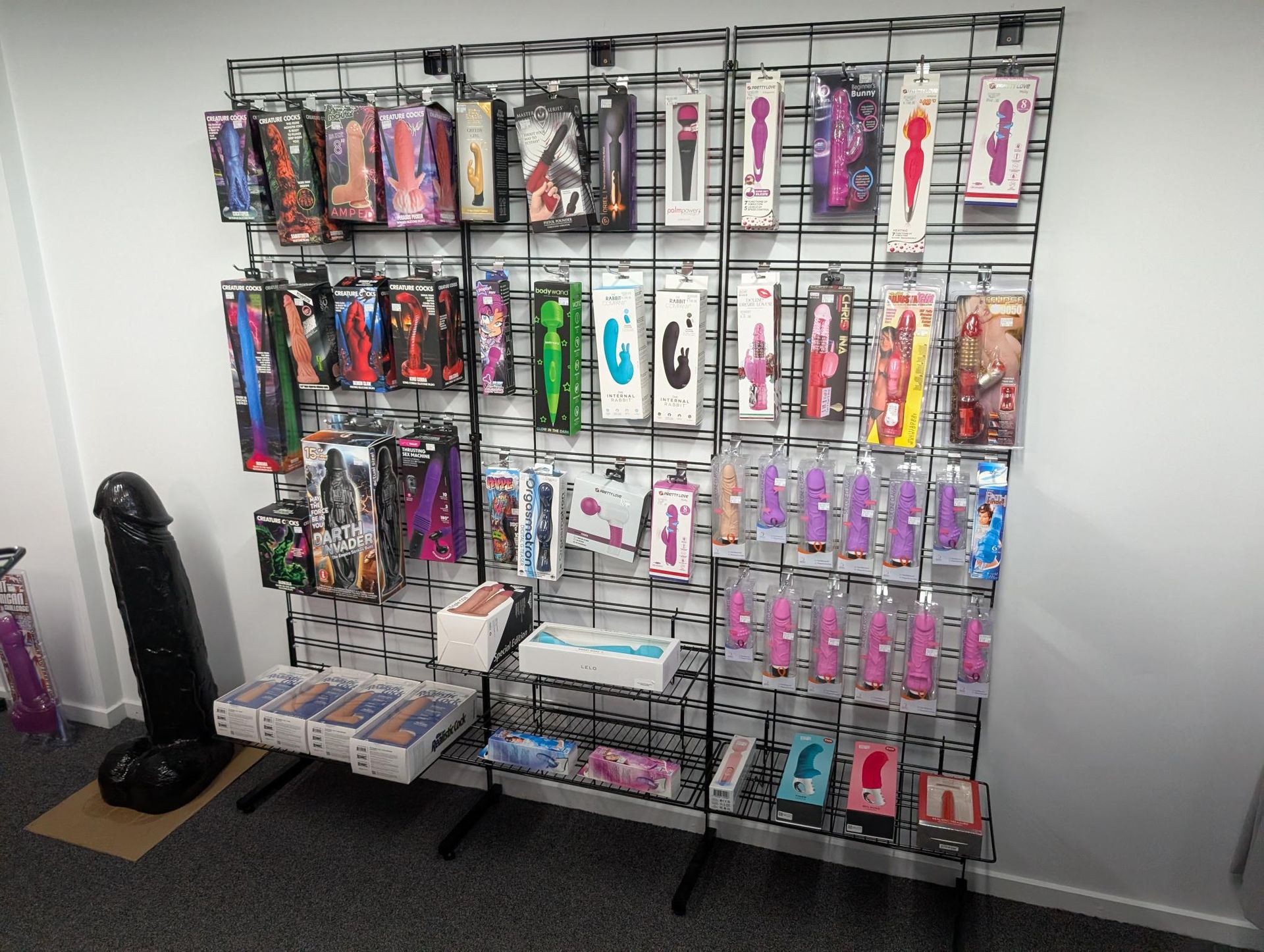A display rack stocked with various intimate products for sale in a retail setting, with a large black model on the floor — A Bit Cheeky The Adult Store In Lismore, NSW