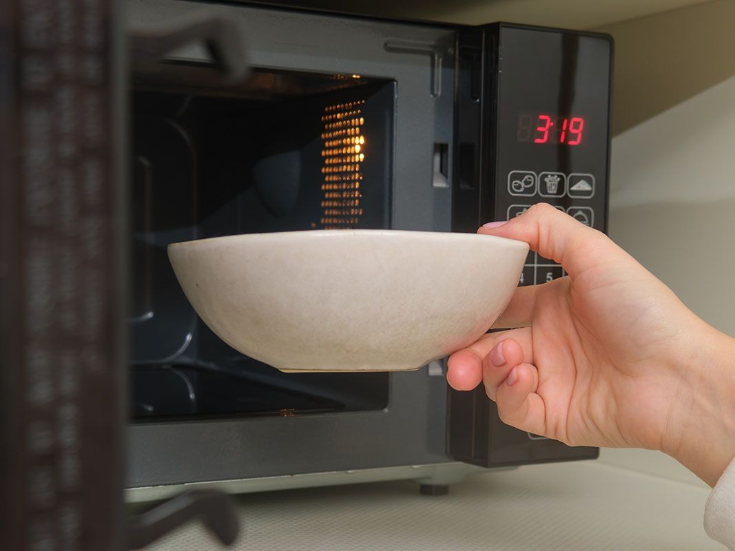 Uma pessoa está tirando uma tigela do micro-ondas.