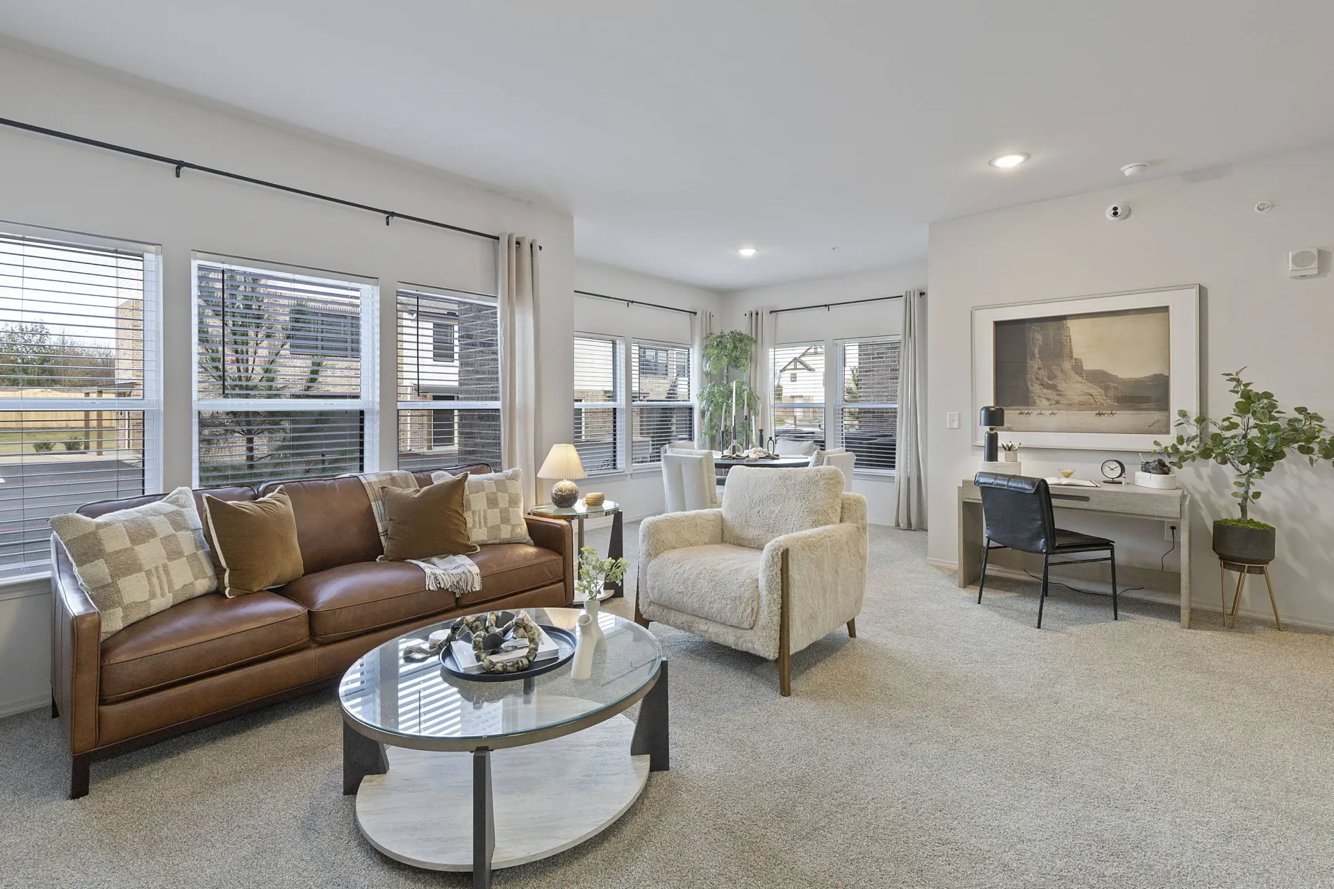 A living room with a brown leather couch, a white chair, and a glass coffee table.
