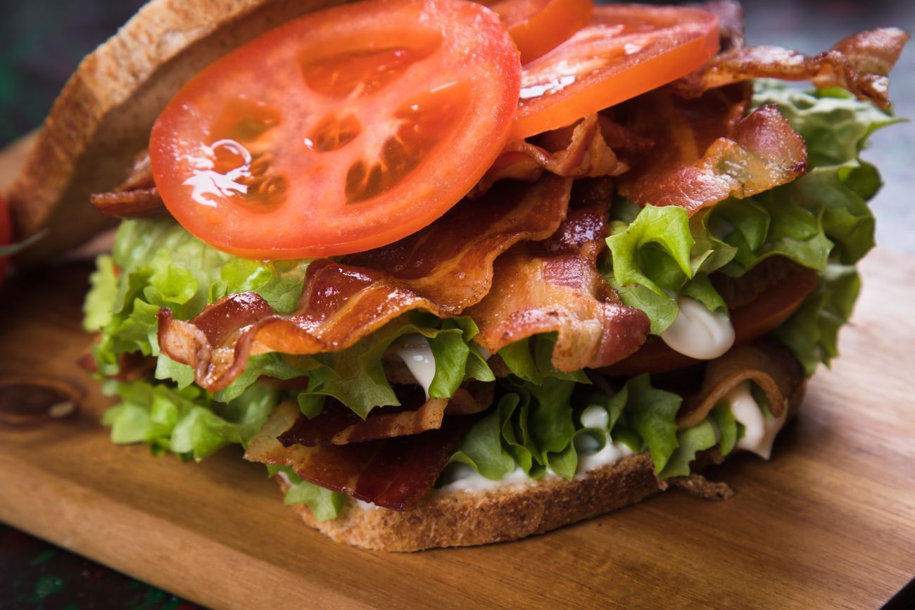 a close up of a sandwich with lettuce , tomatoes , and bacon on a wooden cutting board 