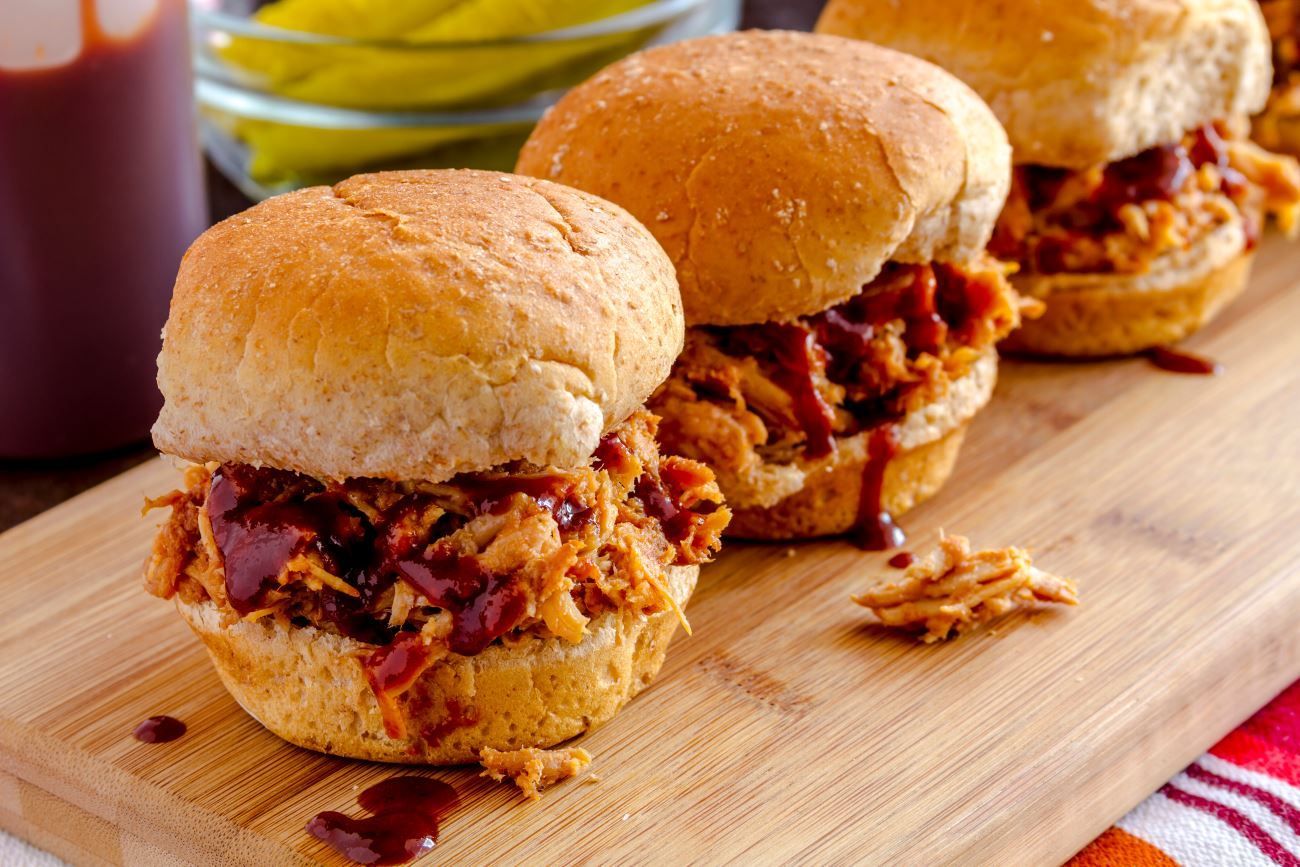 three pulled pork sliders are sitting on a wooden cutting board 