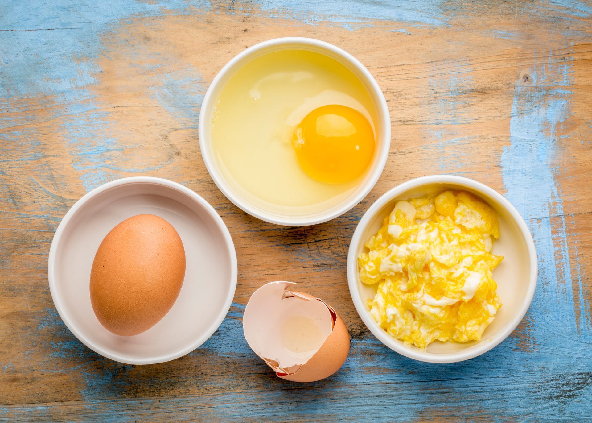 three bowls of eggs and scrambled eggs on a wooden table 