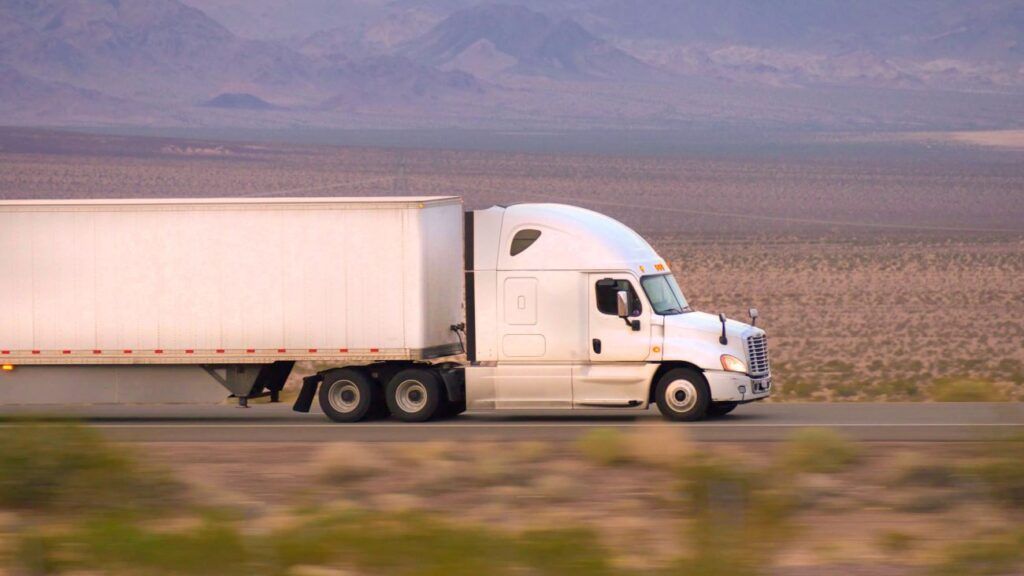 a white semi truck is driving down a desert road .