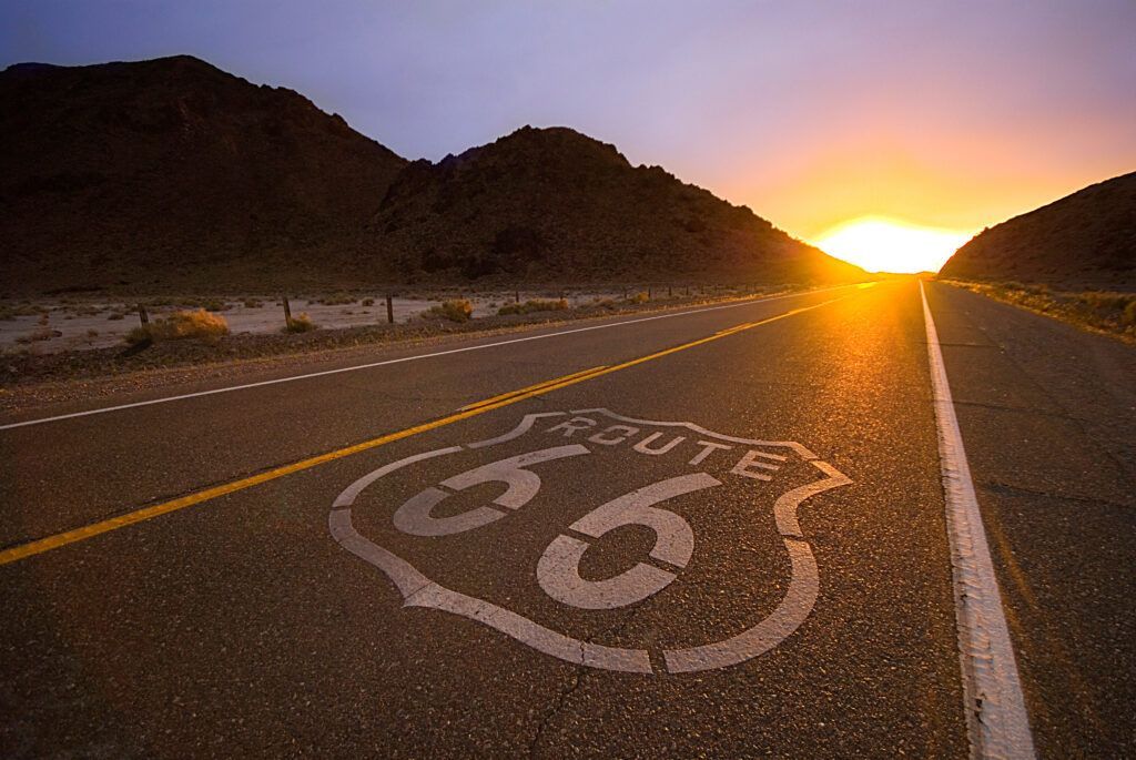 the sun is setting behind the route 66 sign on the road.