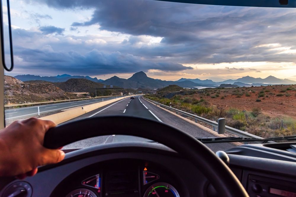 a person is driving a truck down a highway with mountains in the background .