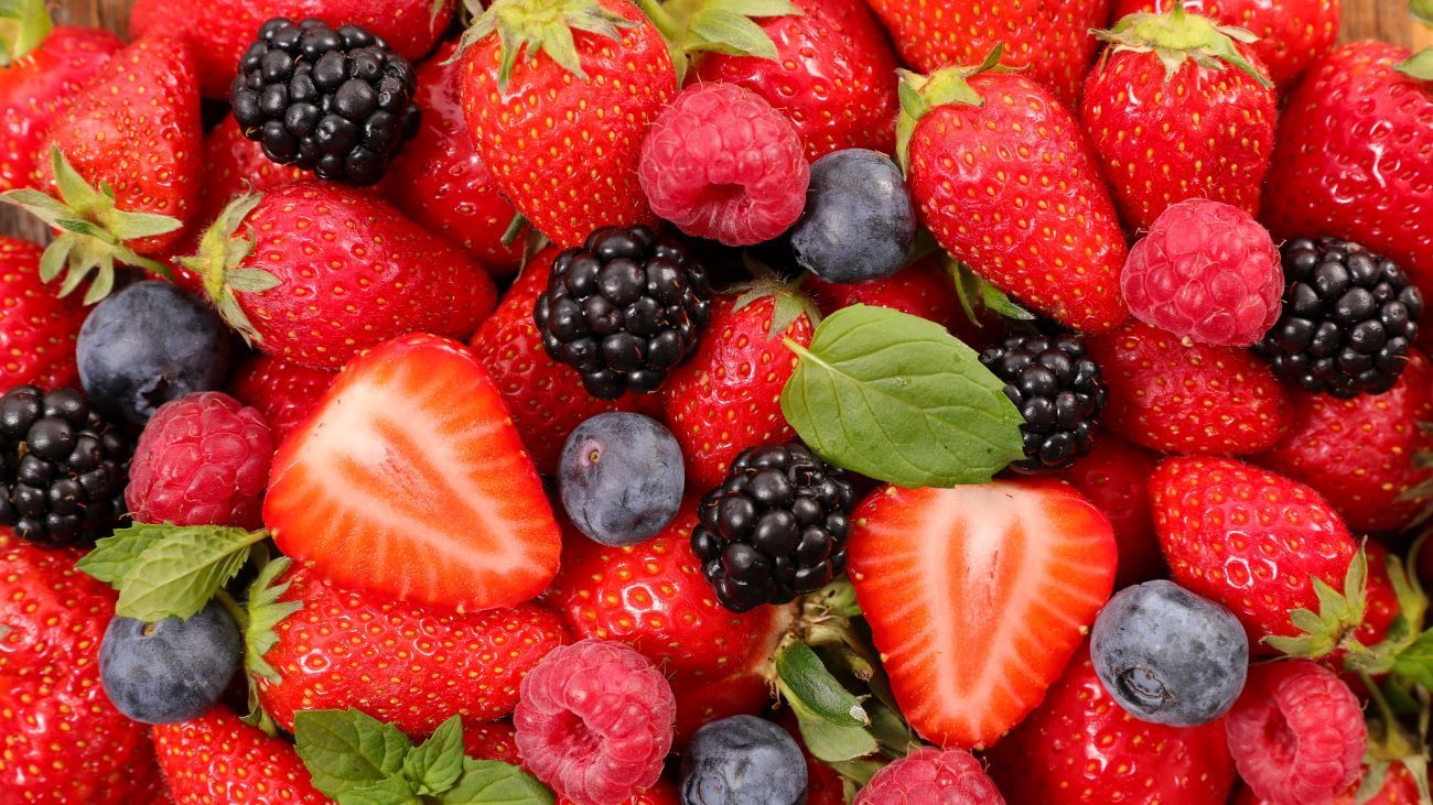 a pile of strawberries , raspberries , blackberries , blueberries and mint leaves .