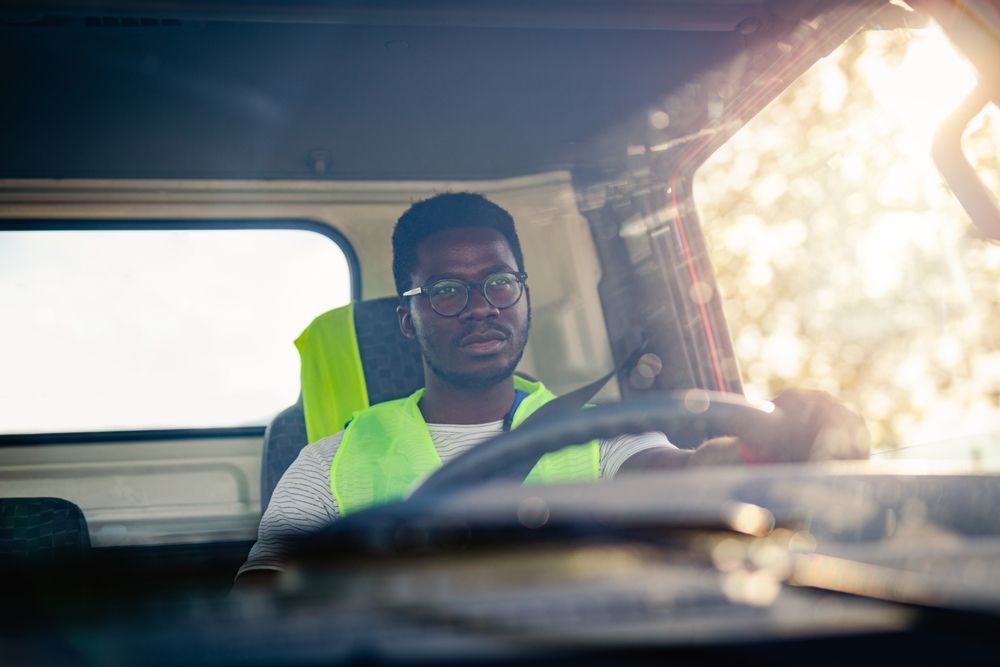a man wearing glasses and a yellow vest is driving a truck .