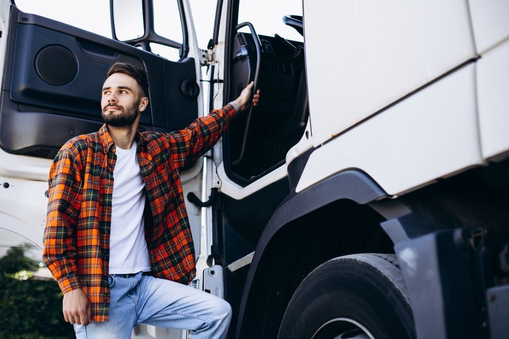 a man in a plaid shirt is standing next to his leased semi truck.