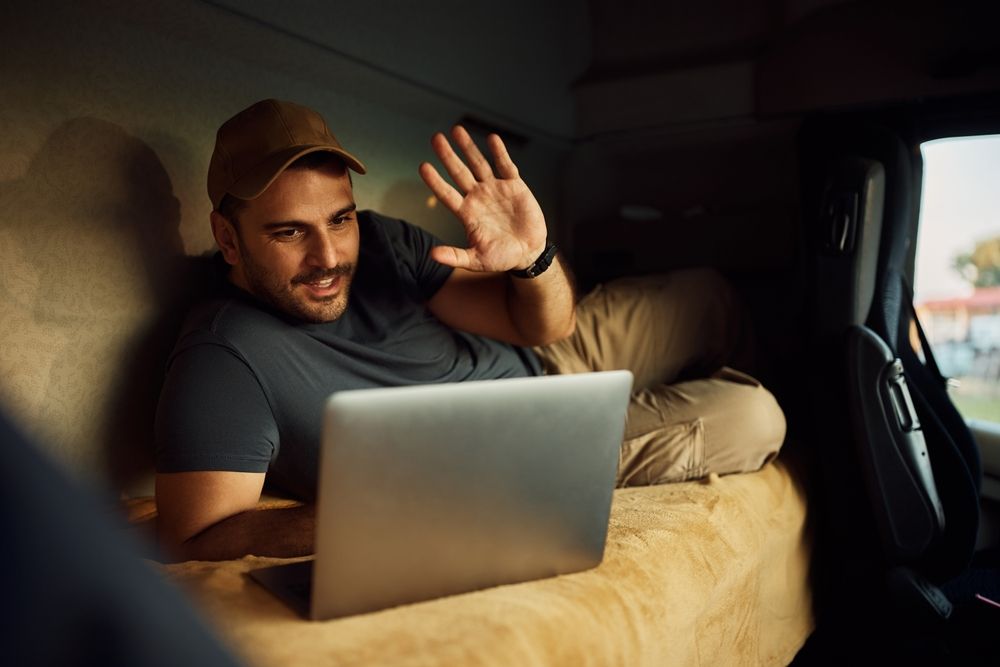 a man is sitting on a bed in a truck using a laptop computer .