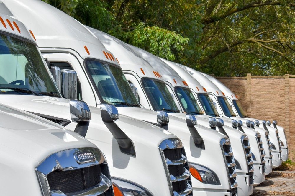 a row of white semi trucks are parked in a parking lot .