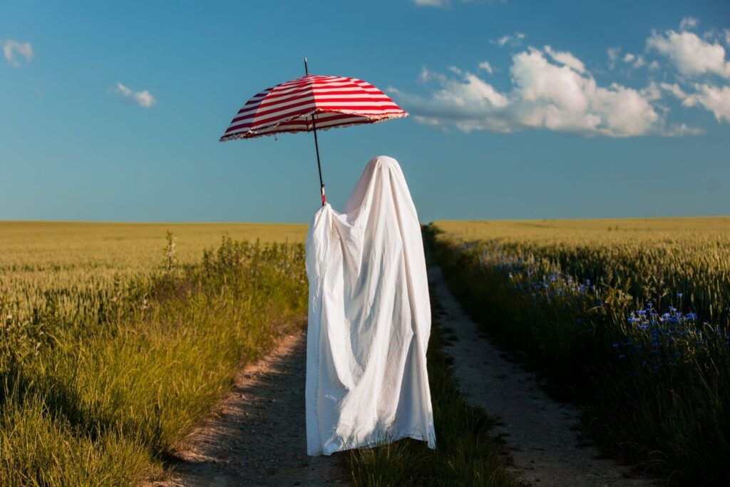 a ghost is walking down a dirt road holding an umbrella .
