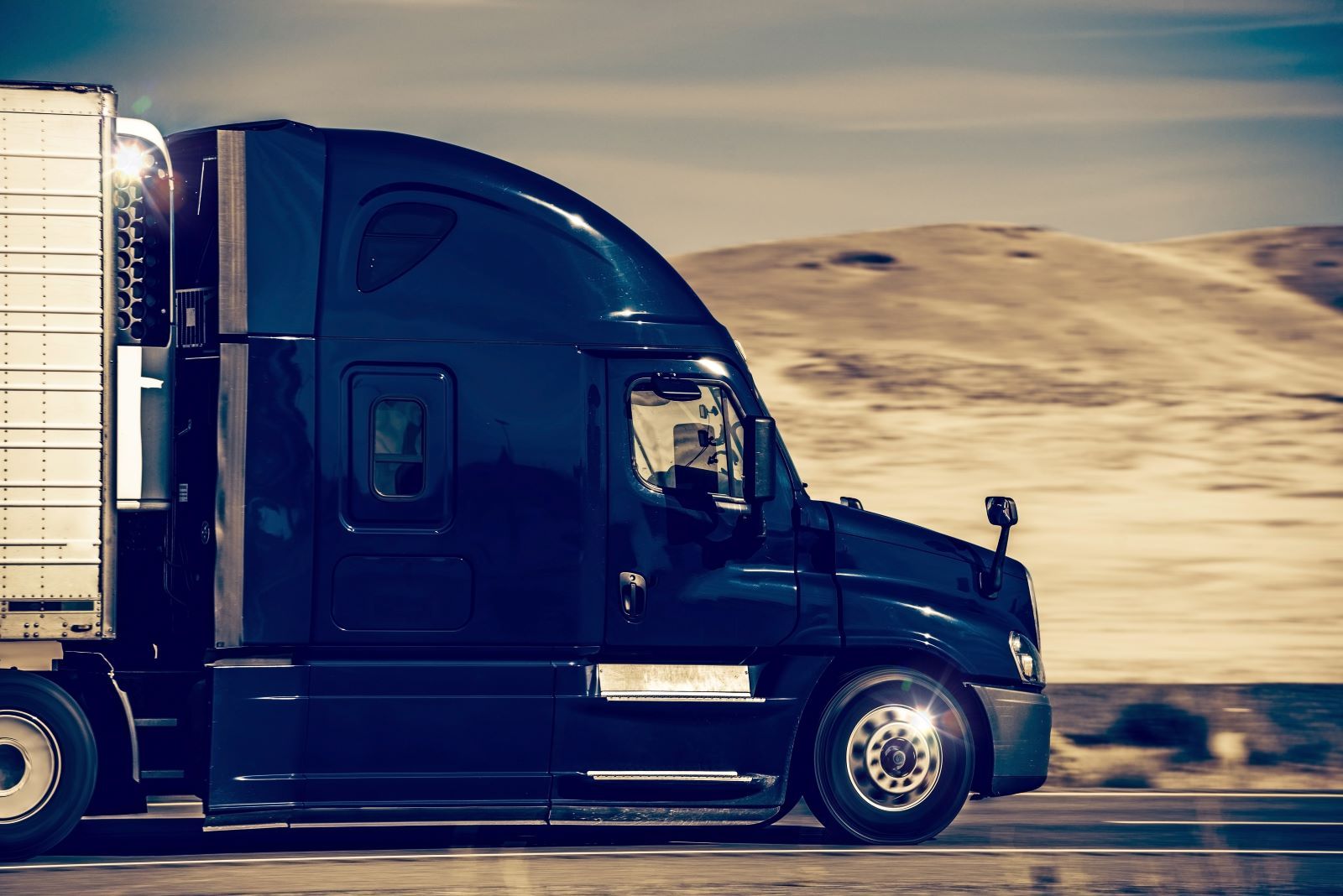 a black semi truck is driving down a highway .