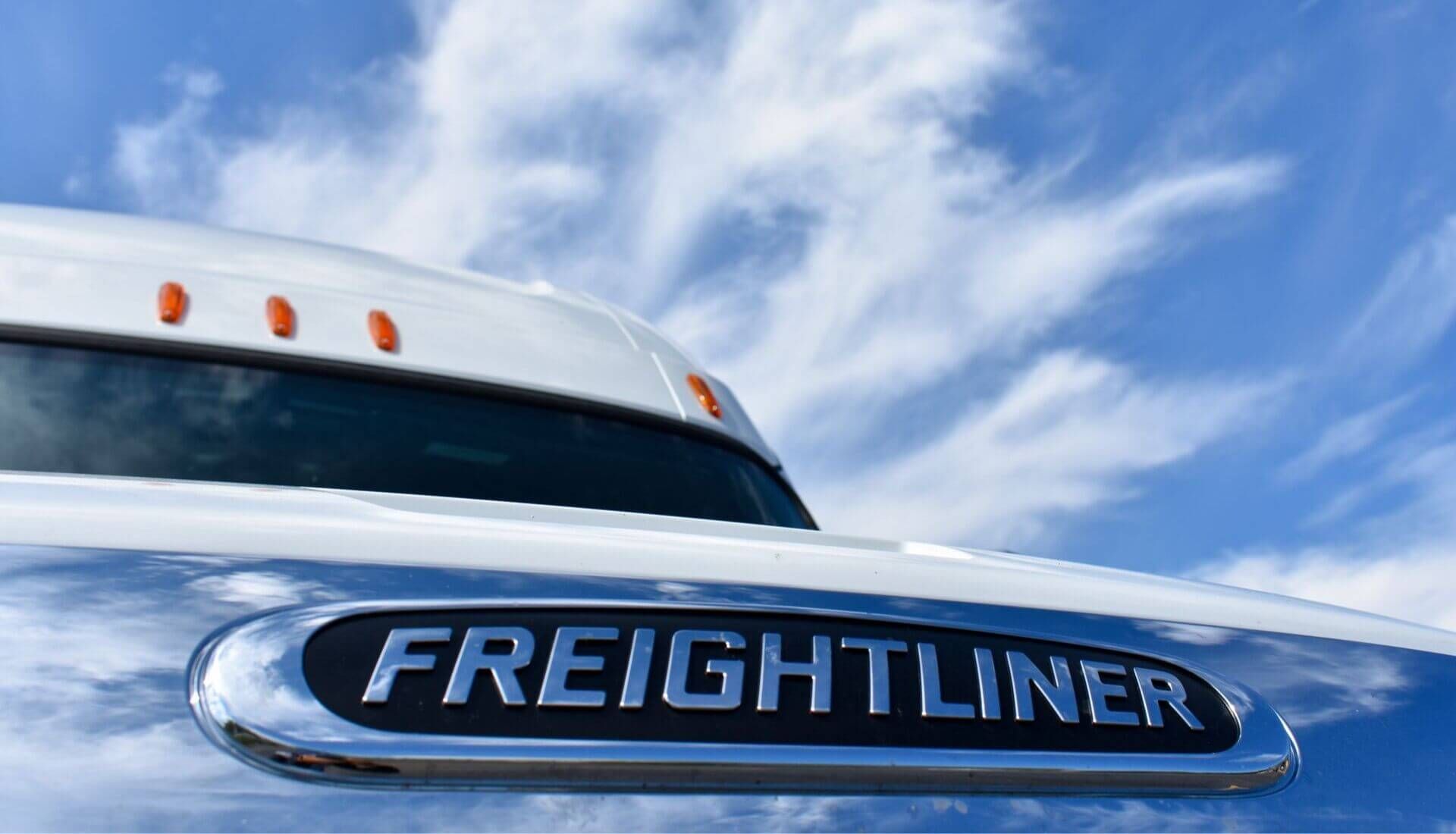 a white freightliner truck is parked in front of a blue sky with clouds.