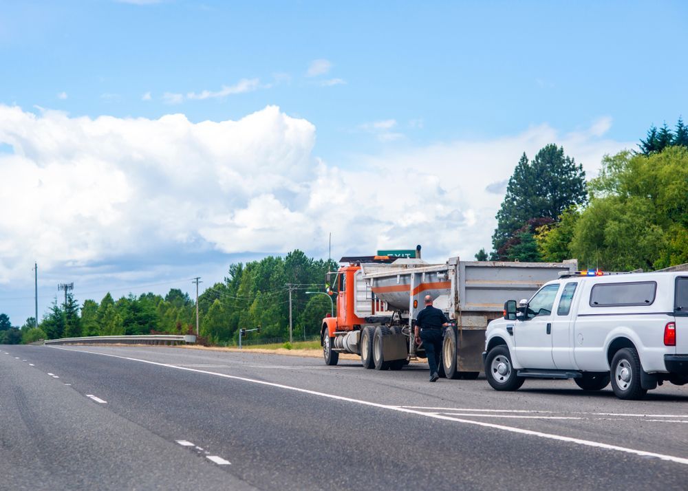 a man is standing next to a dump truck on the side of the road .