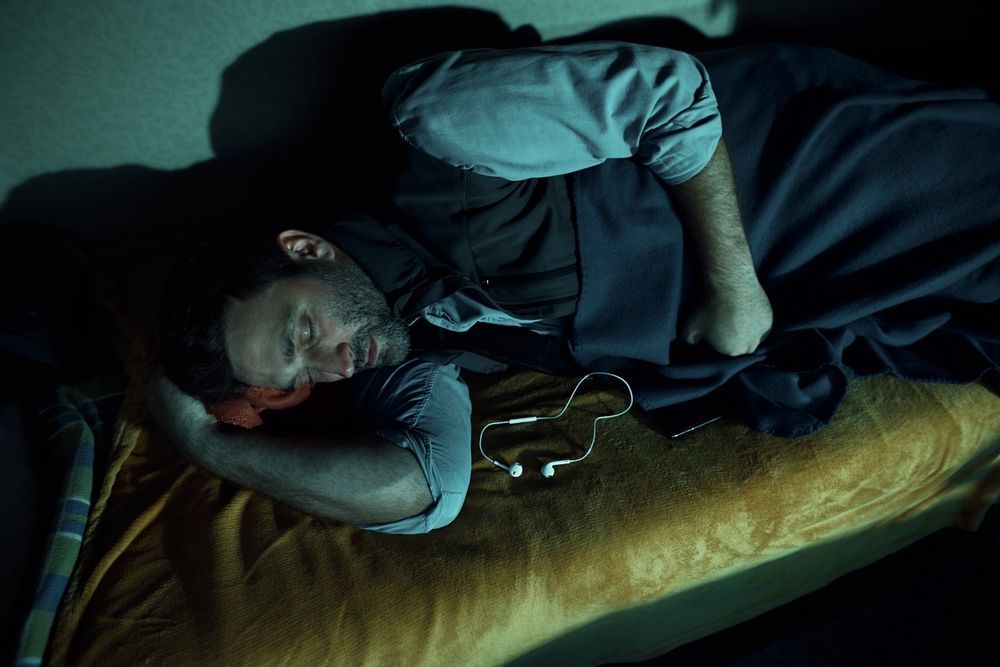 a man is sleeping on a bed with headphones plugged into his ear .