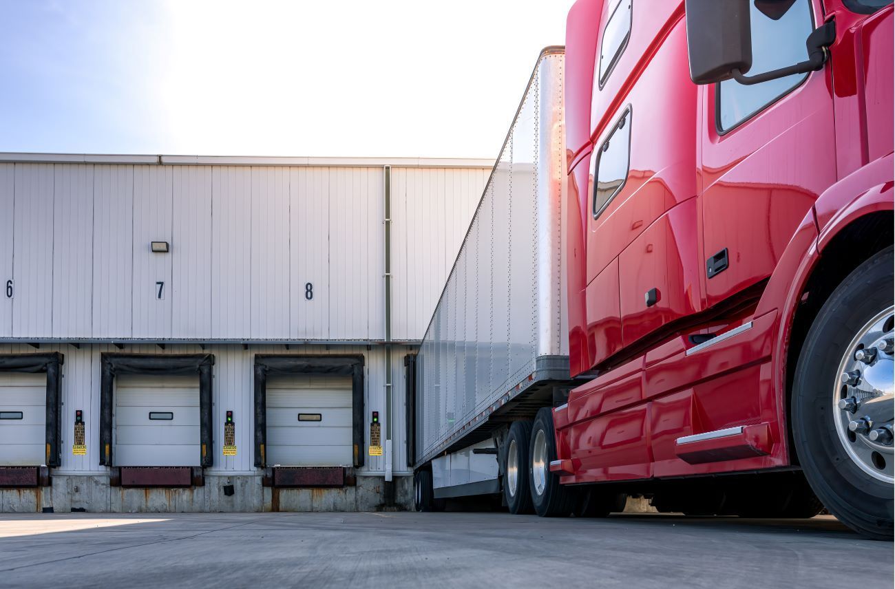 a red semi truck backing up into a warehouse.