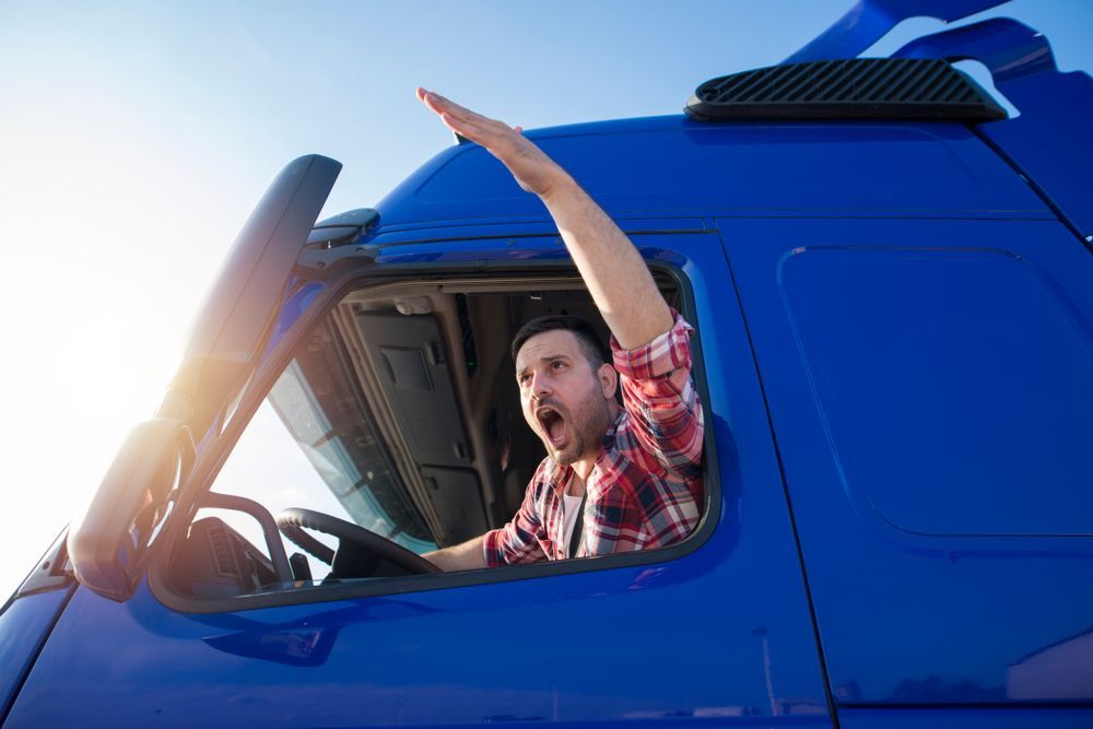 a man is driving a blue semi truck with his hand out the window experiencing road rage.