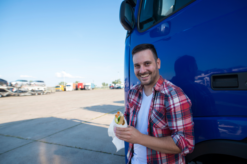 a man is leaning against a blue truck while eating a sandwich .