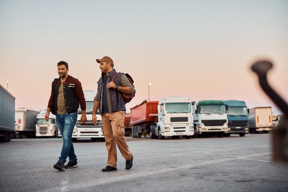 two men are walking in a parking lot next to trucks.