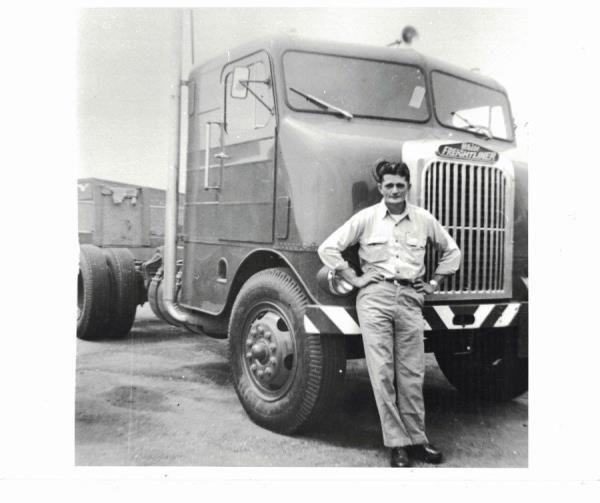 a black and white photo of a man standing in front of a freightliner truck.