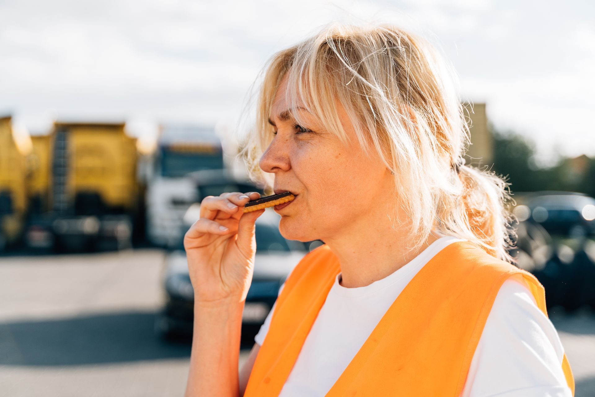 a woman in an orange vest is eating a piece of food .