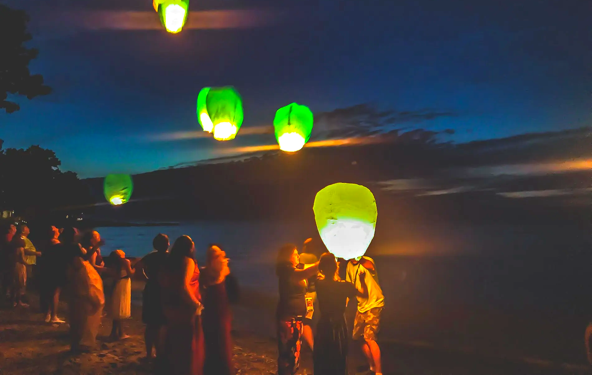 people at beach, lanterns floating in sky at night