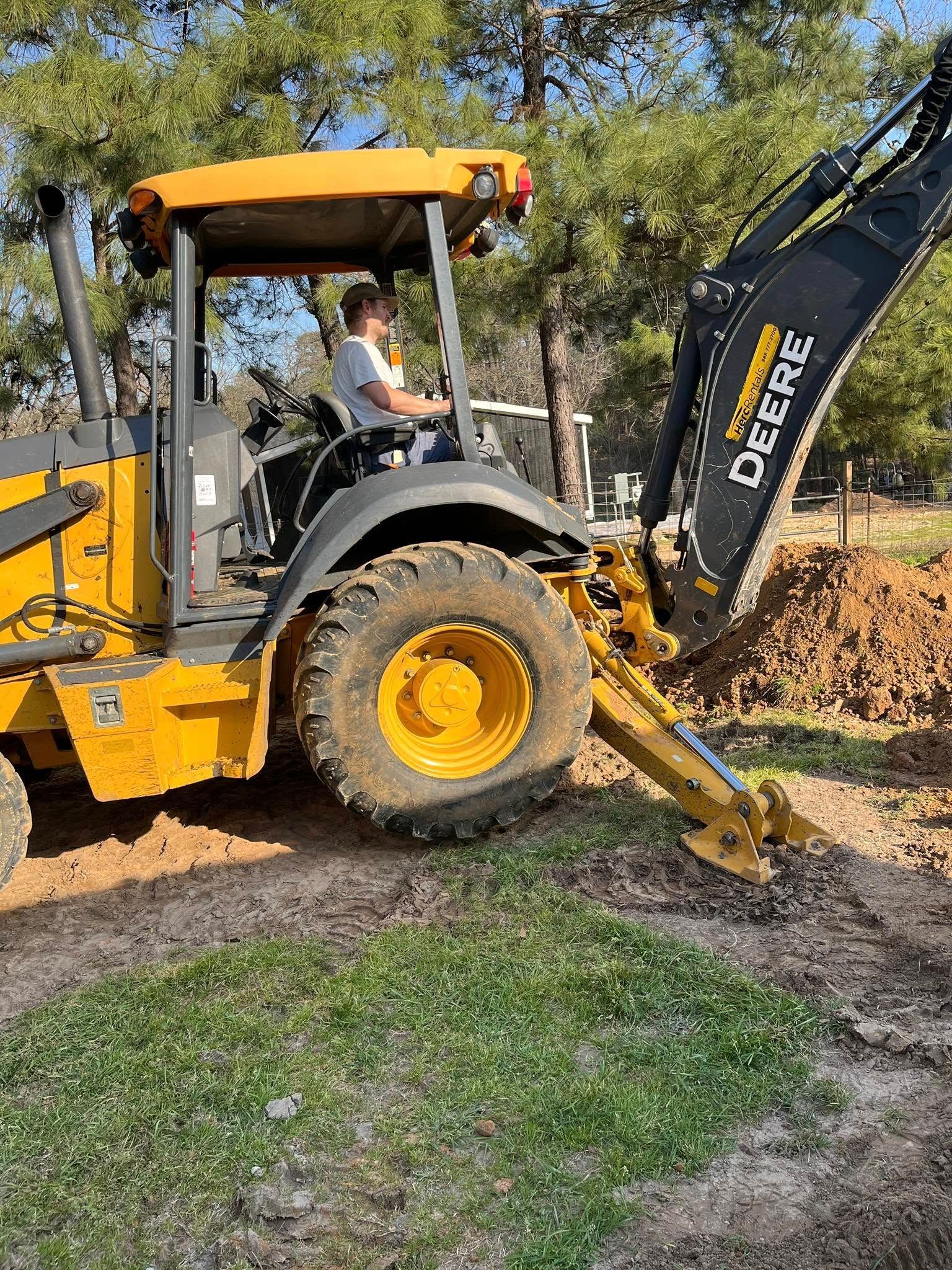 A man is driving a yellow tractor on a dirt road.