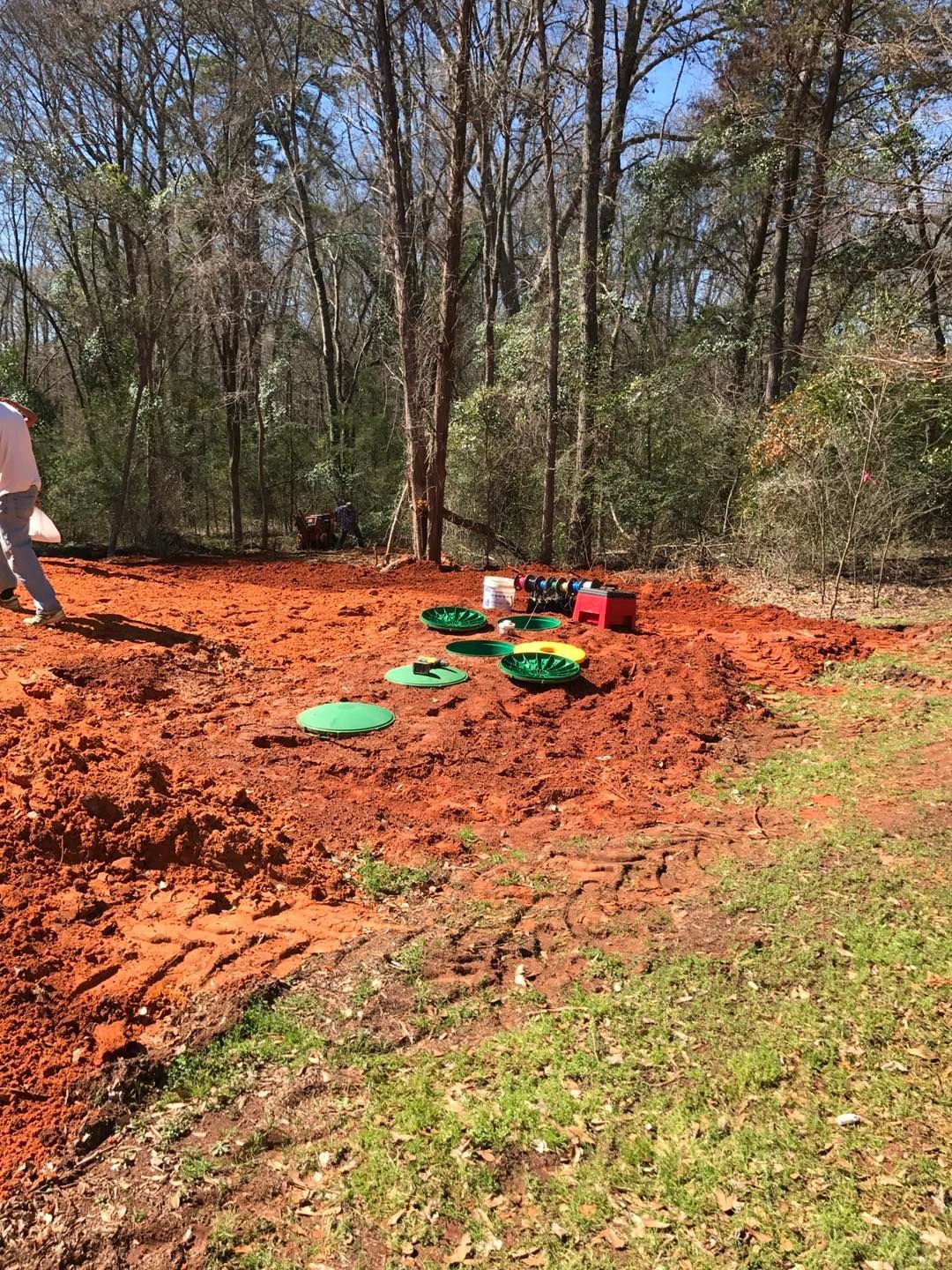 A man is digging in the dirt in a field with trees in the background.