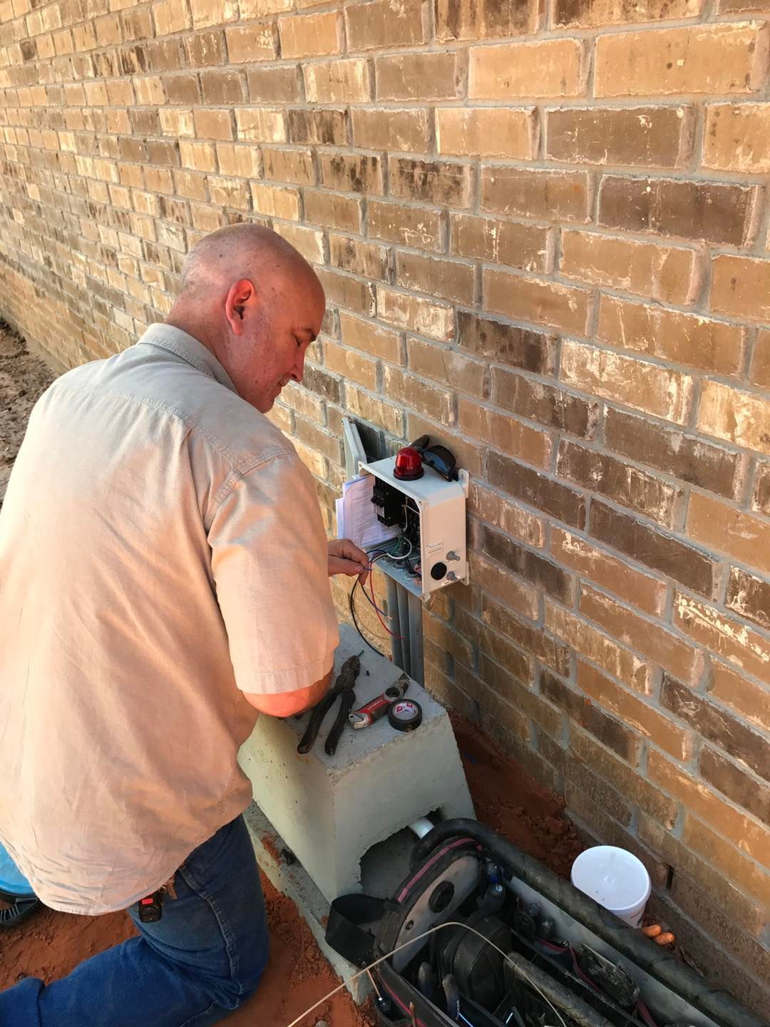 A man is kneeling down in front of a brick wall working on a machine.