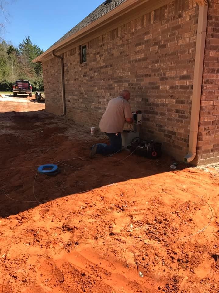 A man is kneeling in the dirt in front of a brick house.