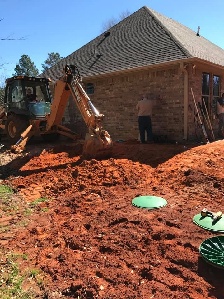 A tractor is digging a hole in the dirt in front of a house.