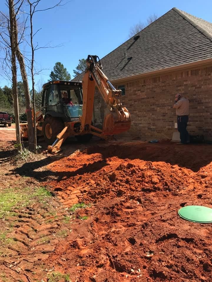 A tractor is digging a hole in the dirt in front of a house.
