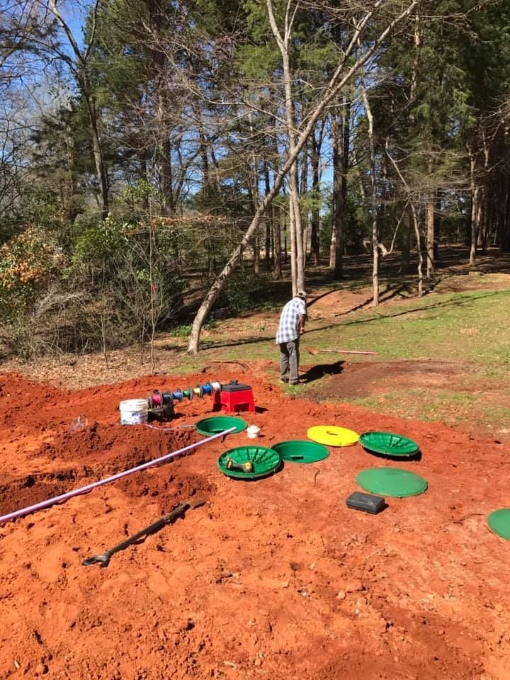A man is working on a septic system in a dirt field.