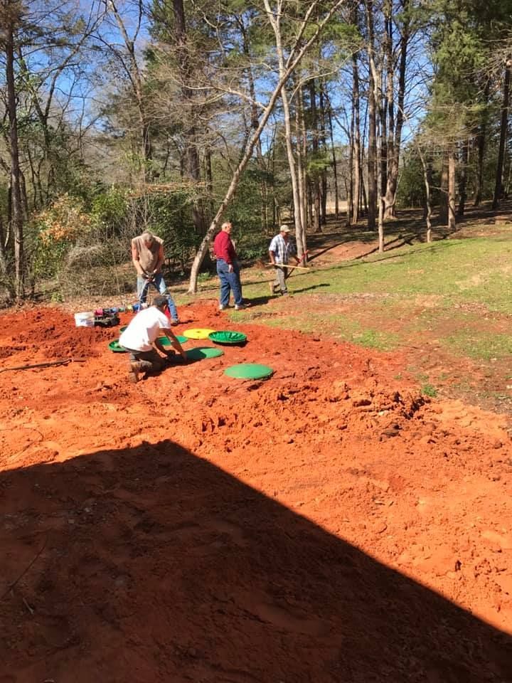 A group of people are working on a dirt field in the woods.