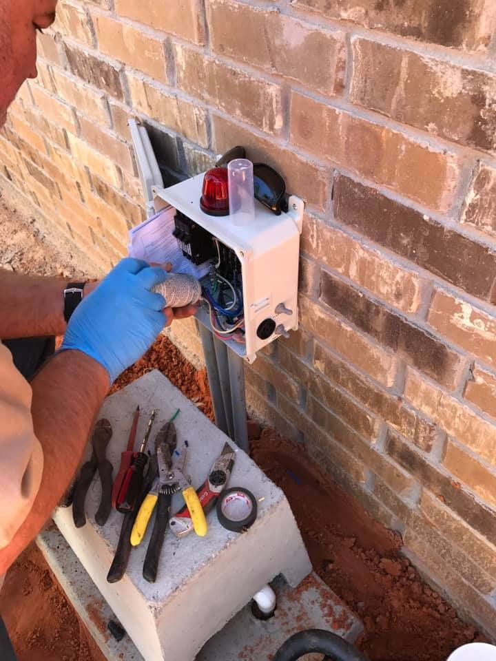 A man is working on an electrical box on a brick wall.