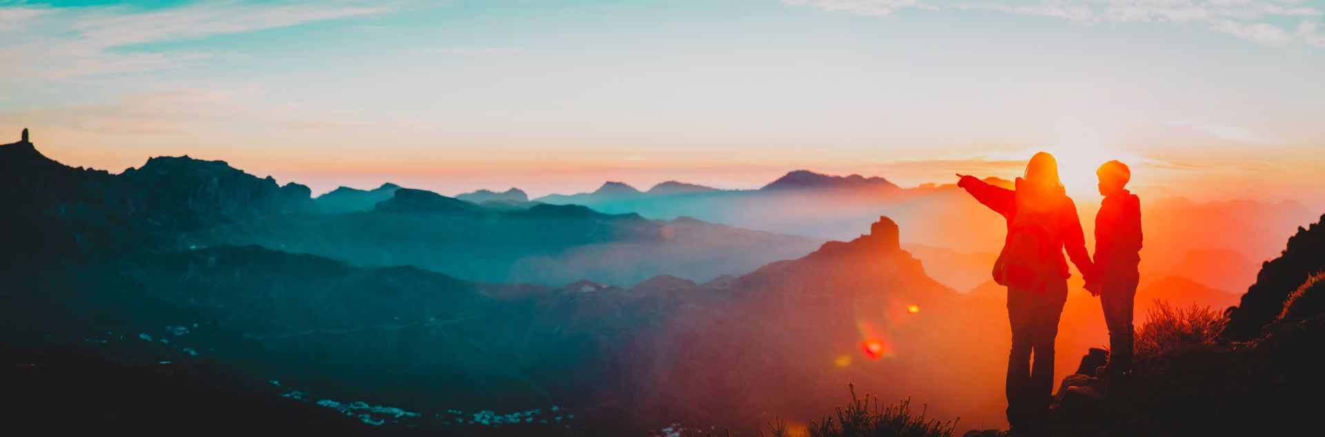 Two people are standing on top of a mountain looking at the sunset.