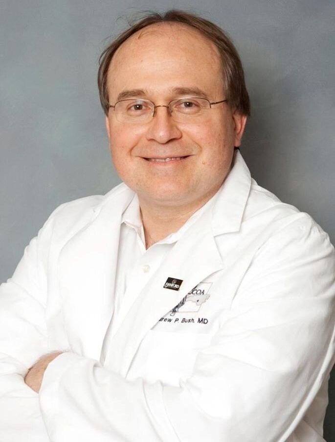 A man wearing glasses and a white lab coat with the name john on it