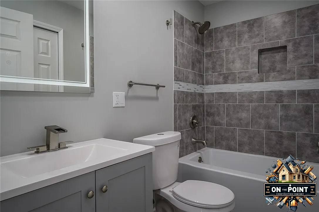 Modern bathroom with gray tile shower, bathtub, toilet, and white vanity sink