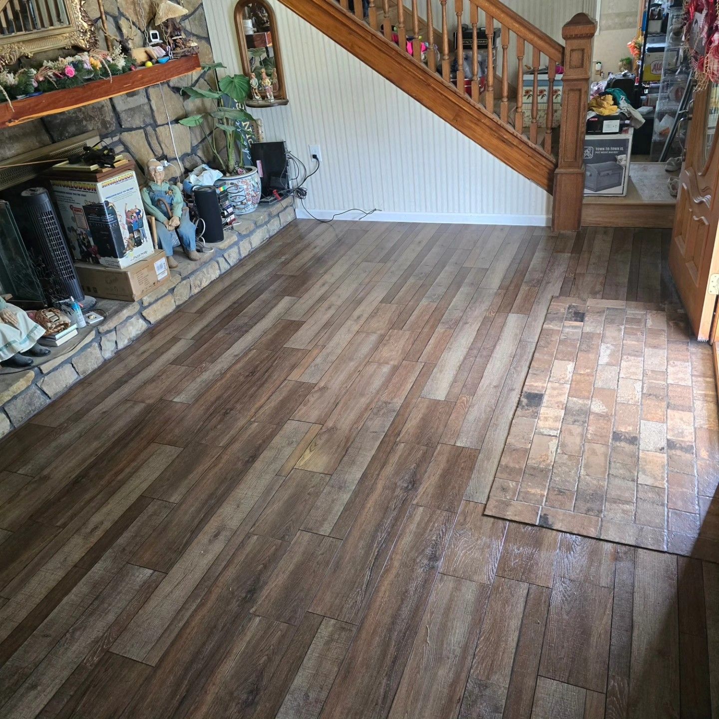 Living room with partially refinished hardwood floor, stone fireplace, and wooden staircase