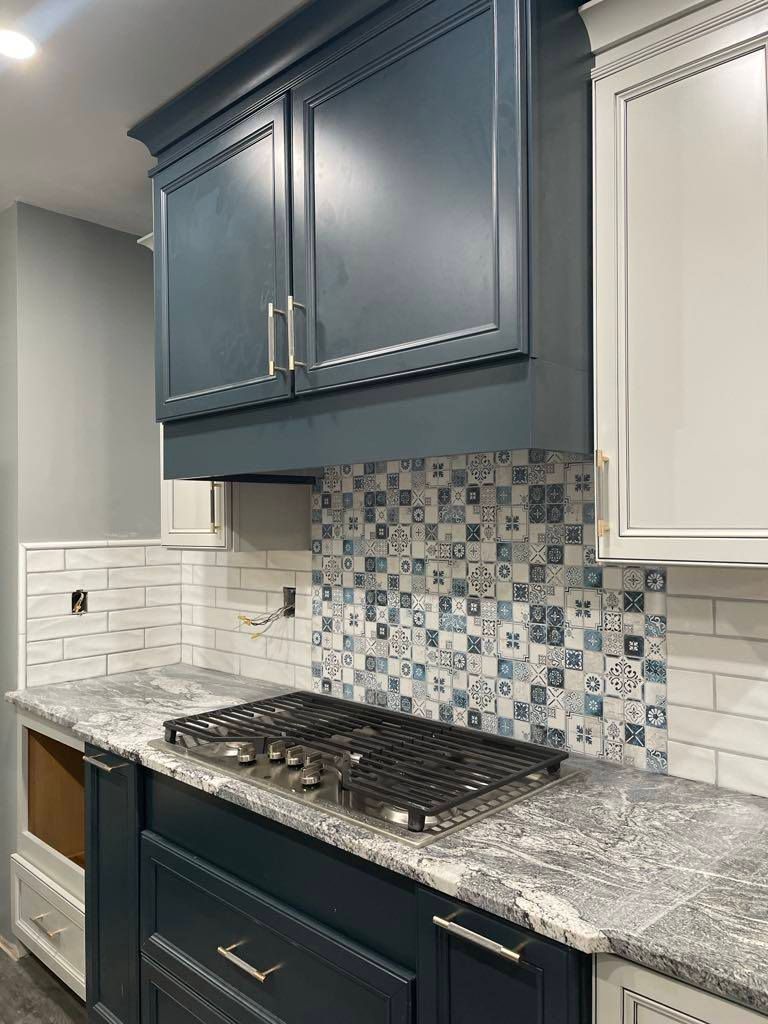 Blue kitchen cabinets above a stovetop with a mosaic tile backsplash and white countertops