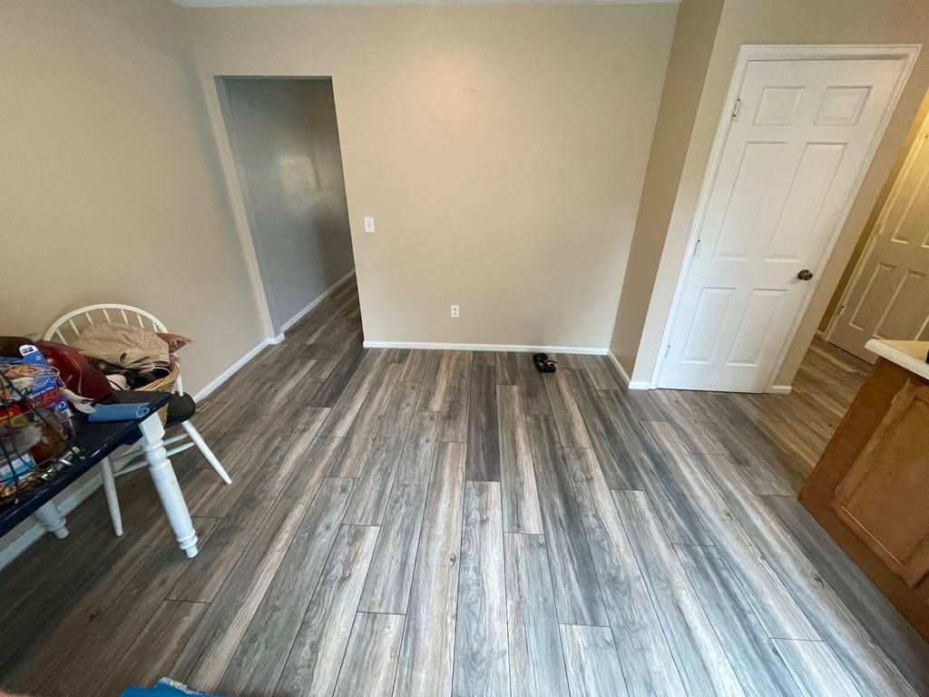 Empty room with gray wood-look flooring, beige walls, and a white door near a doorway and cabinet.