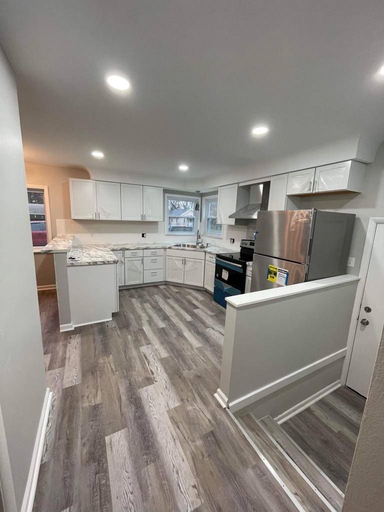 Bright modern kitchen with white cabinets, gray wood floors, and stainless steel appliances