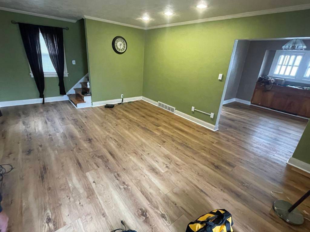 Empty living room with green walls, wood flooring, and an open doorway to another room.