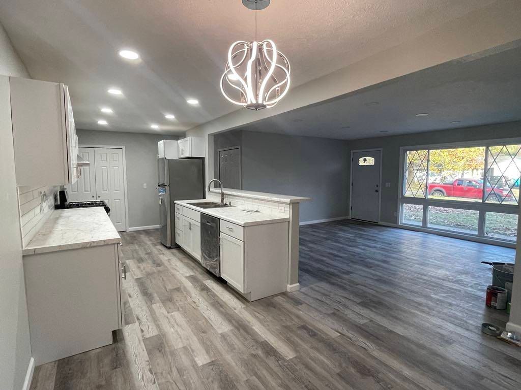 Modern kitchen with island, white cabinets, gray wood floors, and large sliding glass doors